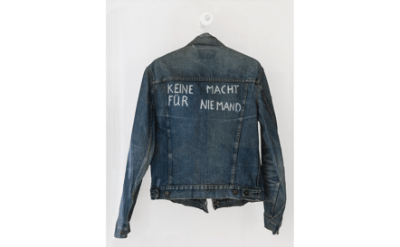 Eine Jacke aus dunklem Jeansstoff, auf deren Rücken in weißer Schrift steht: „Keine Macht für Niemand“